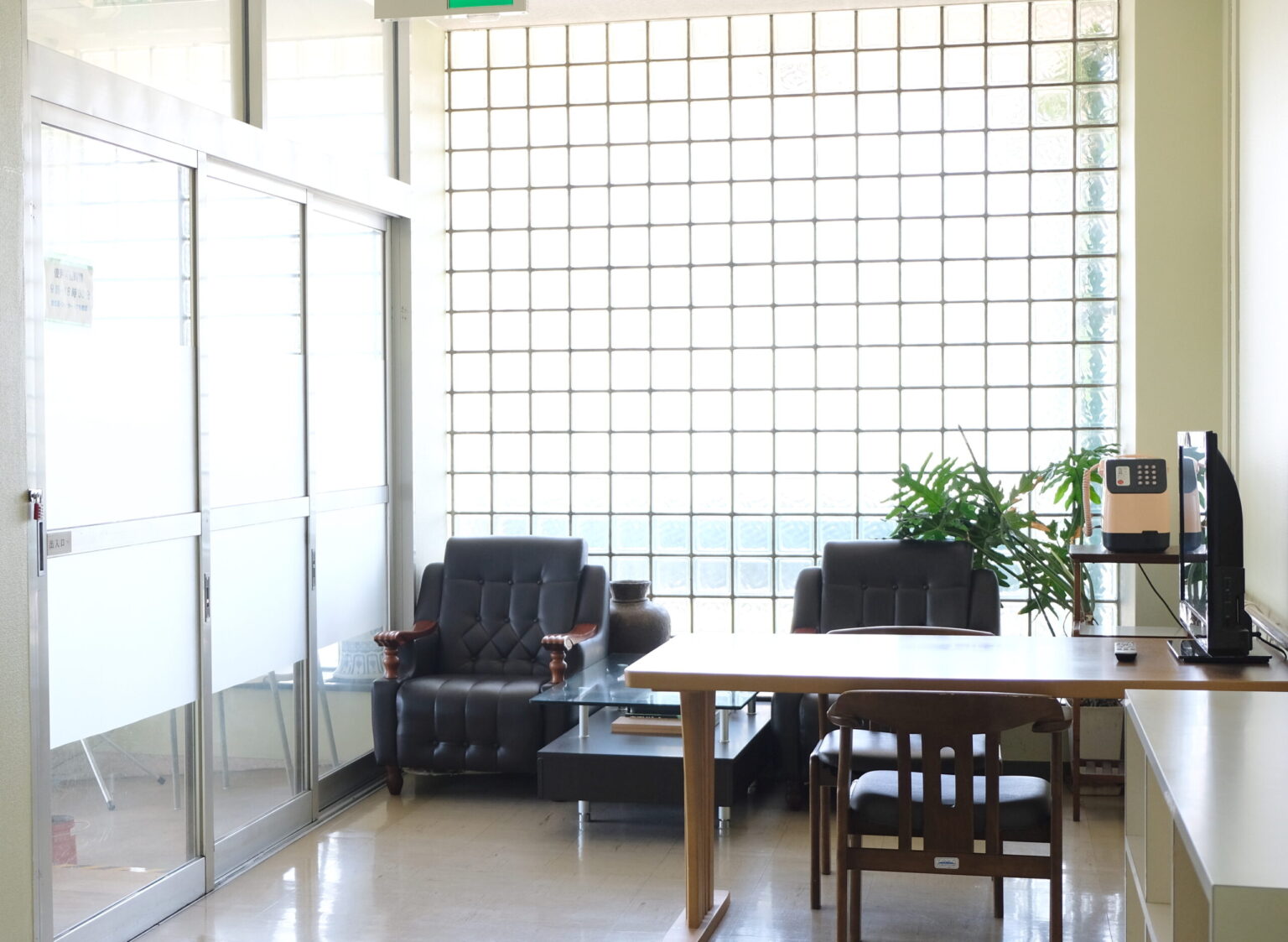 施設の共用スペース。黒いソファとテーブル、観葉植物が配置された落ち着いた談話室。